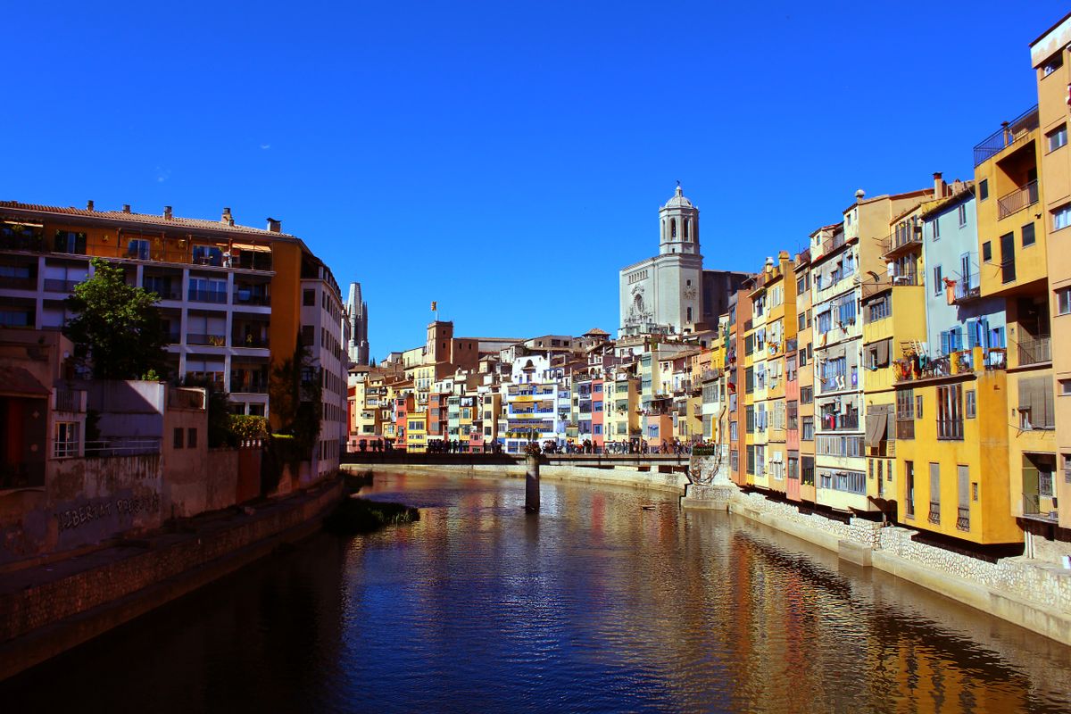 The colourful ochre and yellow riverside houses of Girona lining the Onyar river with the cathedral tower behind