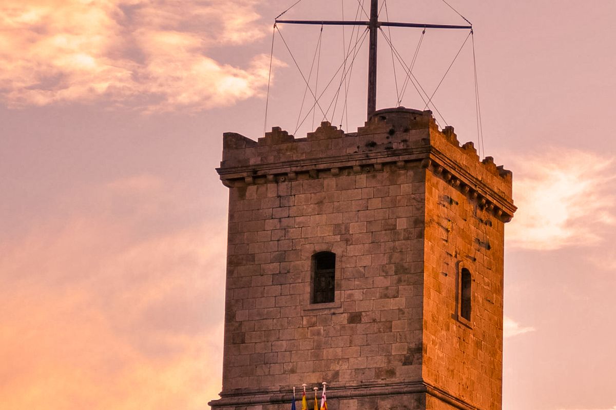 The crenellated stone watchtower of Montjuïc Castle catching golden evening light with flags below